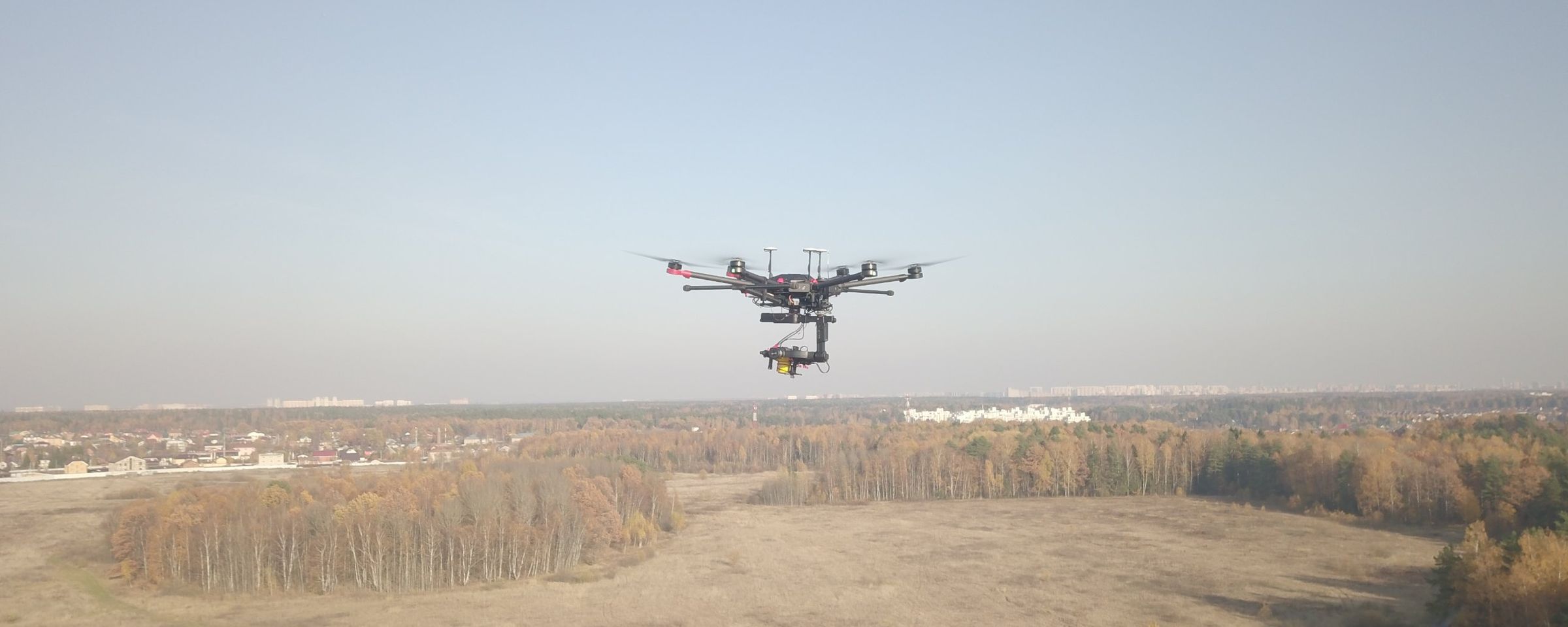 Hexacopter in flight over open fields, with the yellow LASER FALCON on a gimbal underneath